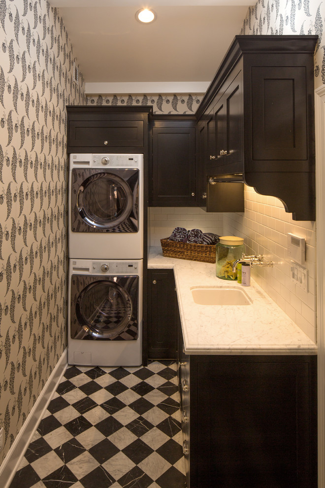 Inspiration for a small traditional l-shaped dedicated laundry room in Los Angeles with black cabinets, a stacked washer and dryer, an undermount sink, shaker cabinets, multi-coloured walls, multi-coloured floor and white benchtop.