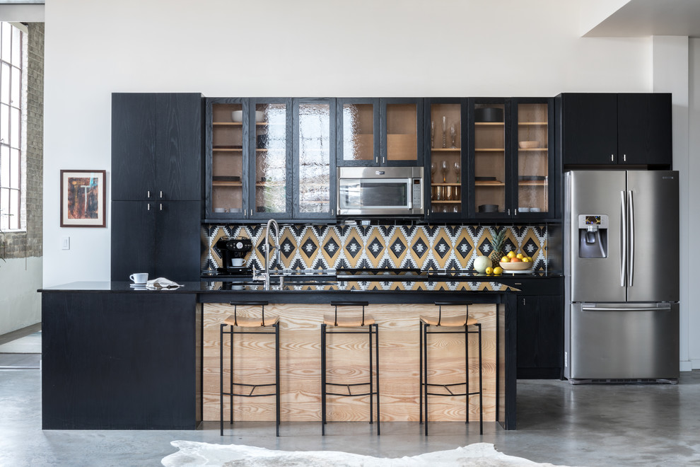 Photo of an expansive industrial single-wall open plan kitchen in New Orleans with black cabinets, multi-coloured splashback, ceramic splashback, stainless steel appliances, concrete floors, with island, grey floor, black benchtop and glass-front cabinets.