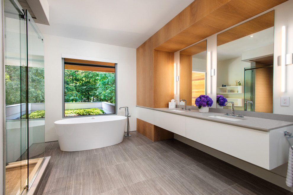 Design ideas for a large contemporary master bathroom in New York with flat-panel cabinets, white cabinets, a freestanding tub, white walls, an undermount sink, grey floor, grey benchtops, engineered quartz benchtops and a sliding shower screen.