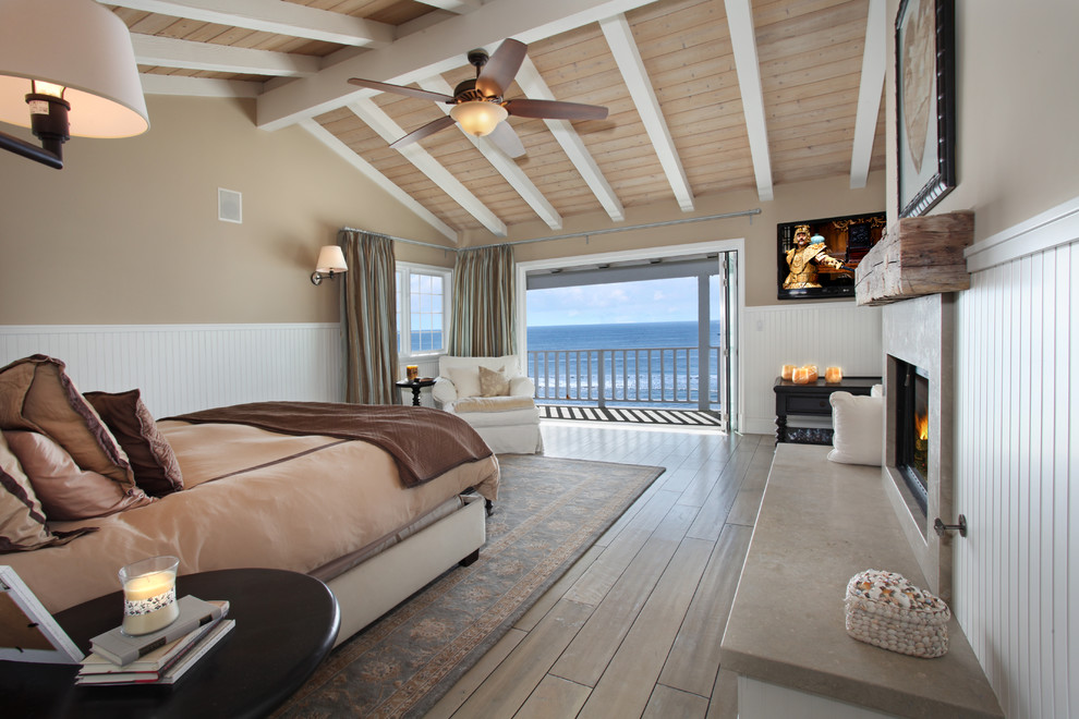 Inspiration for a beach style bedroom in Orange County with beige walls, a standard fireplace and light hardwood floors.