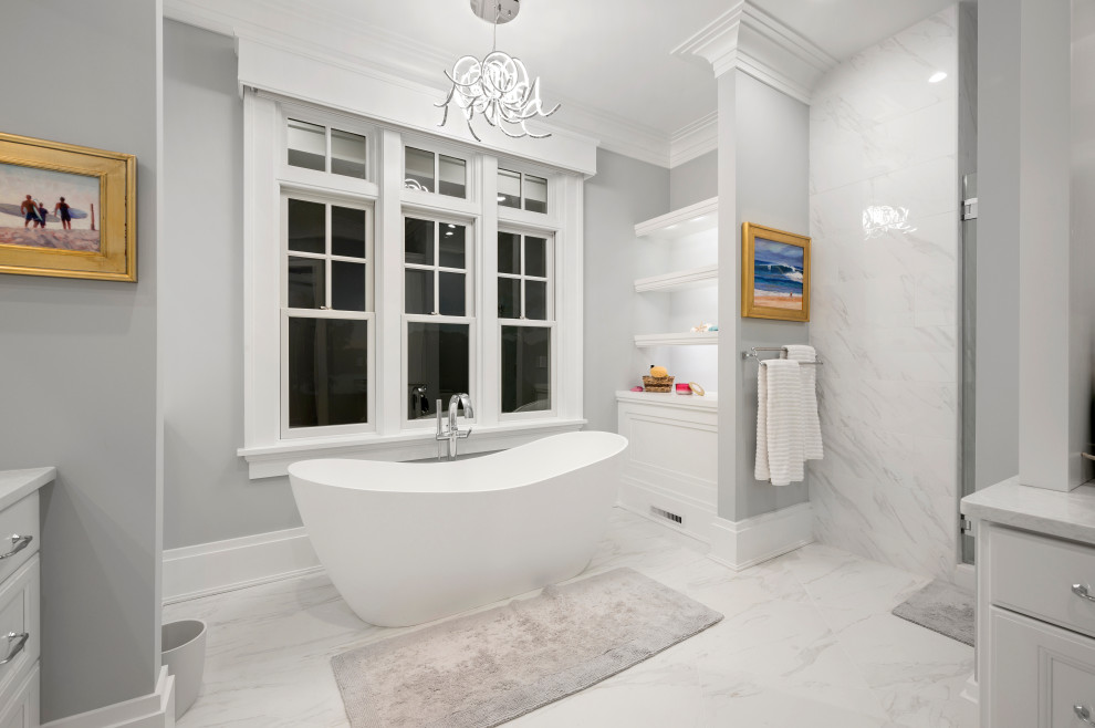 This is an example of a large beach style master bathroom in Other with furniture-like cabinets, white cabinets, a freestanding tub, a shower/bathtub combo, gray tile, porcelain tile, grey walls, marble floors, an undermount sink, engineered quartz benchtops, white floor, a hinged shower door, white benchtops, a double vanity and a built-in vanity.