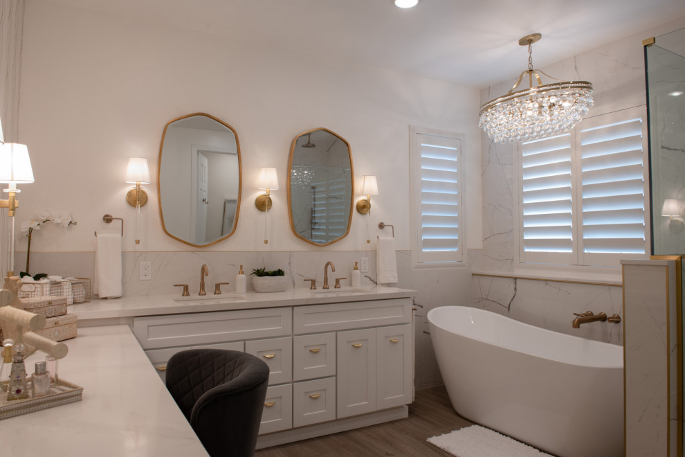 Photo of a large traditional ensuite bathroom in San Diego with recessed-panel cabinets, white cabinets, a freestanding bath, a corner shower, white tiles, marble tiles, medium hardwood flooring, a submerged sink, engineered stone worktops, brown floors, a hinged door, white worktops, double sinks and a built in vanity unit.