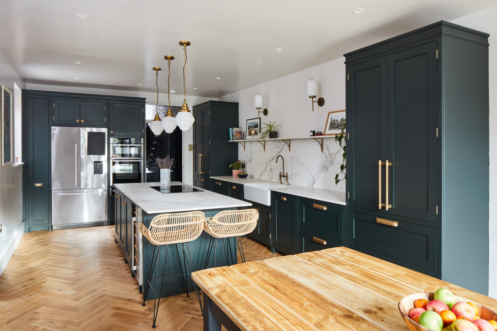 Photo of a mid-sized traditional single-wall eat-in kitchen in London with a farmhouse sink, shaker cabinets, green cabinets, quartzite benchtops, grey splashback, engineered quartz splashback, stainless steel appliances, dark hardwood floors, with island, brown floor and grey benchtop.