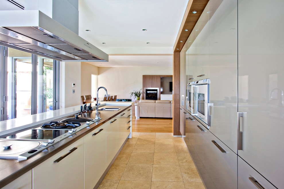 Photo of a contemporary galley kitchen pantry in Perth with an integrated sink, flat-panel cabinets, medium wood cabinets, stainless steel benchtops, glass sheet splashback, stainless steel appliances, ceramic floors and no island.