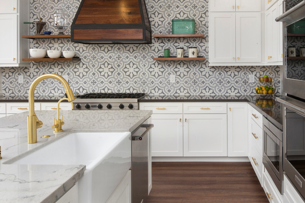 Design ideas for a mid-sized transitional l-shaped eat-in kitchen in Sacramento with a farmhouse sink, shaker cabinets, white cabinets, grey splashback, cement tile splashback, stainless steel appliances, dark hardwood floors, with island, marble benchtops and brown floor.