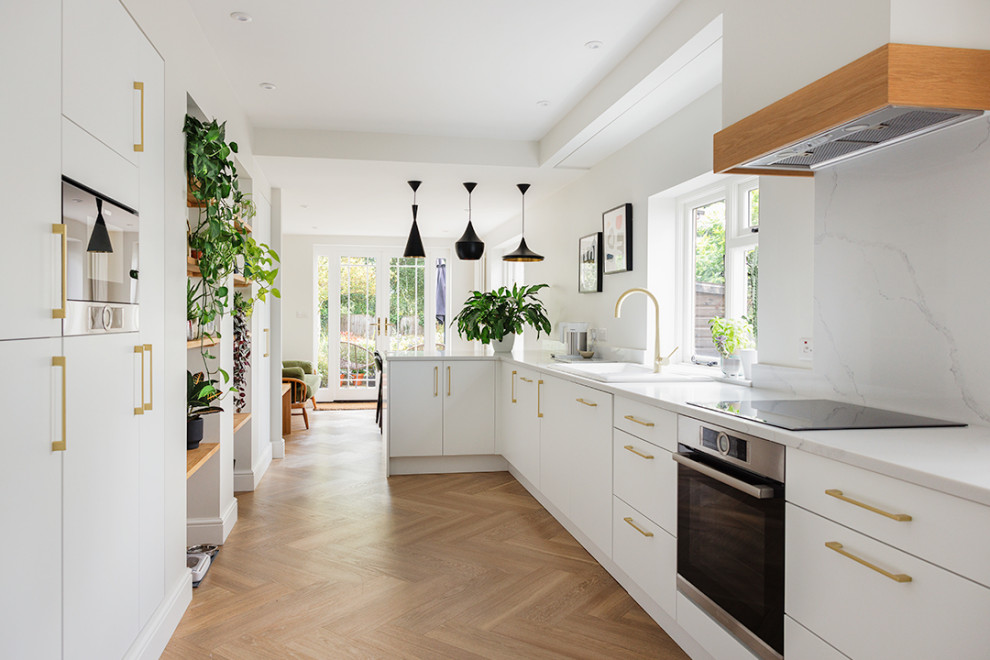 Medium sized modern grey and white galley kitchen/diner with flat-panel cabinets, white cabinets, engineered stone countertops, beige splashback, engineered quartz splashback, black appliances, a breakfast bar, white worktops and feature lighting.