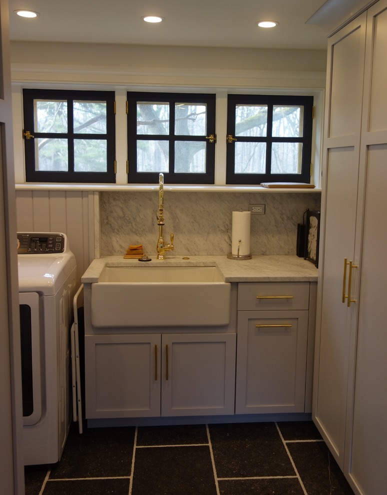 Inspiration for a small transitional galley dedicated laundry room in Philadelphia with a farmhouse sink, shaker cabinets, grey cabinets, marble benchtops, white walls, slate floors, a side-by-side washer and dryer and grey floor.