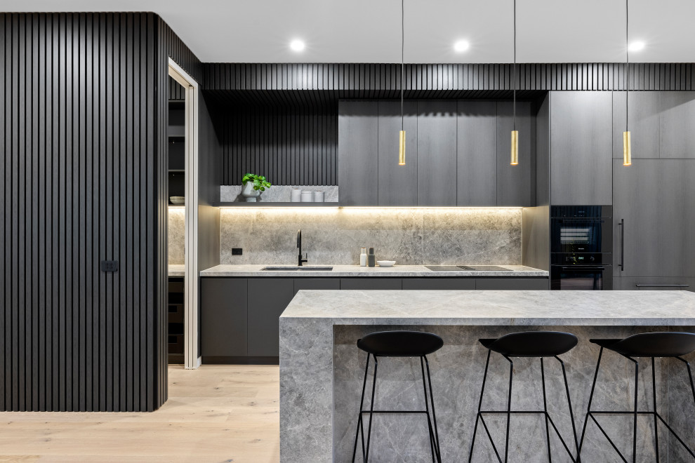 Photo of a mid-sized contemporary galley eat-in kitchen in Melbourne with a double-bowl sink, dark wood cabinets, marble benchtops, grey splashback, marble splashback, black appliances, light hardwood floors, with island and grey benchtop.