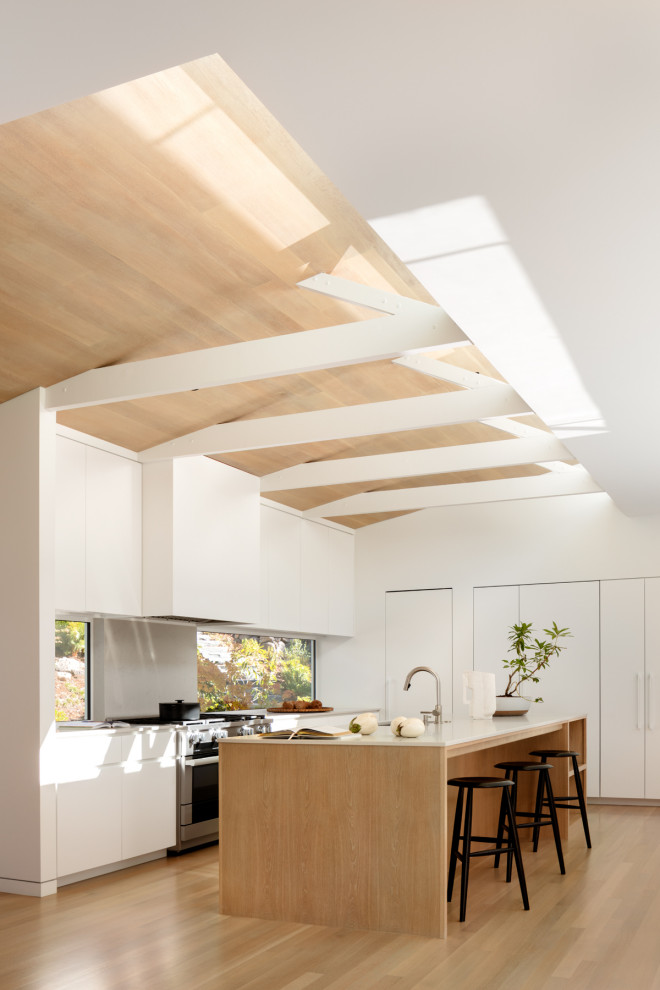 Contemporary u-shaped open plan kitchen in San Francisco with an undermount sink, flat-panel cabinets, white cabinets, quartz benchtops, window splashback, panelled appliances, medium hardwood floors, with island, brown floor, white benchtop, exposed beam, vaulted and wood.