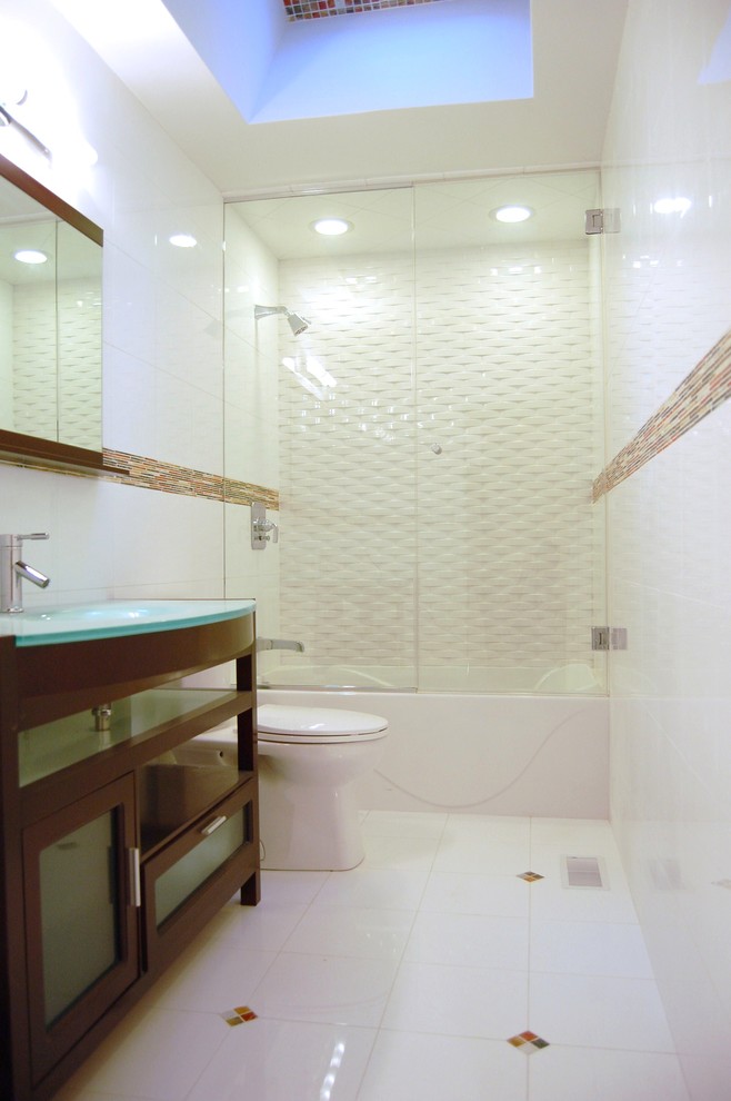 This is an example of a large contemporary 3/4 bathroom in Austin with glass-front cabinets, dark wood cabinets, an alcove tub, a shower/bathtub combo, a two-piece toilet, white tile, porcelain tile, white walls, porcelain floors, an integrated sink, glass benchtops, white floor, a hinged shower door and blue benchtops.