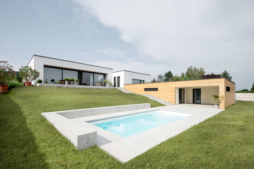 Large modern side yard rectangular pool in Nuremberg with concrete pavers and a pool house.