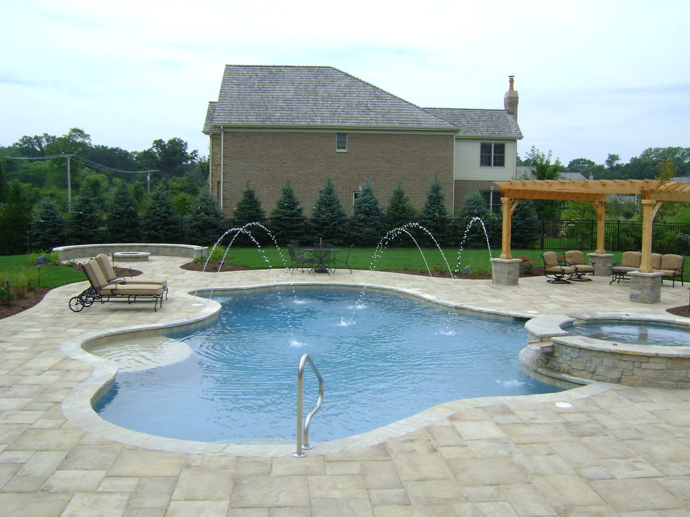 This is an example of a mid-sized traditional backyard custom-shaped natural pool in Chicago with a hot tub and concrete pavers.