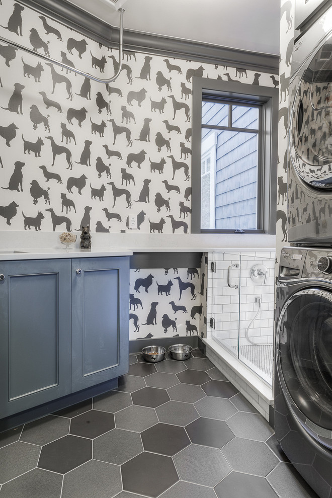 Inspiration for a mid-sized transitional l-shaped utility room in Seattle with an undermount sink, shaker cabinets, blue cabinets, quartz benchtops, grey walls, porcelain floors and a stacked washer and dryer.