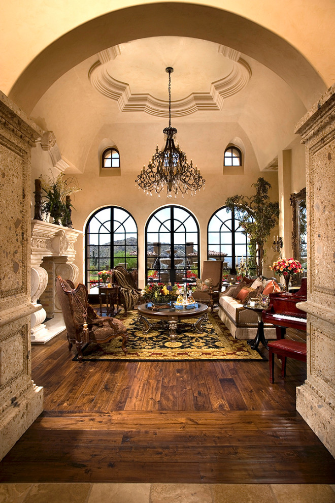 This is an example of a large mediterranean formal enclosed living room in Phoenix with beige walls, dark hardwood floors, a standard fireplace, brown floor, a concrete fireplace surround and vaulted.