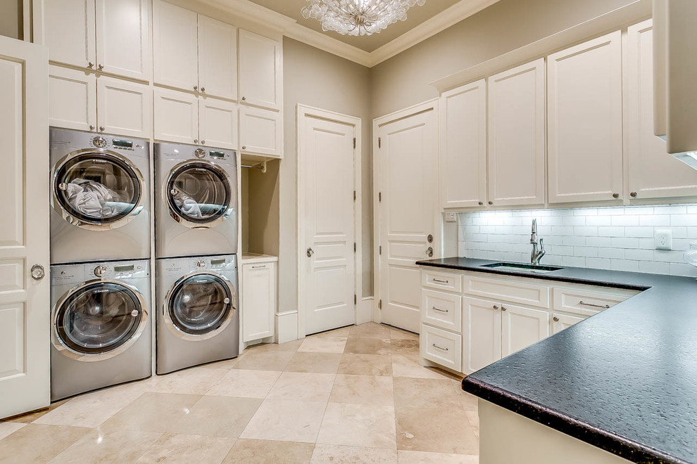 Inspiration for a large traditional u-shaped dedicated laundry room in Dallas with beige walls, porcelain floors, a stacked washer and dryer, recessed-panel cabinets, white cabinets, soapstone benchtops, beige floor, black benchtop and an undermount sink.