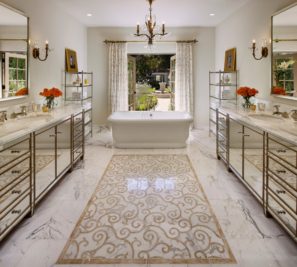 This is an example of a mediterranean bathroom in Santa Barbara with an undermount sink, glass-front cabinets, marble benchtops and a freestanding tub.