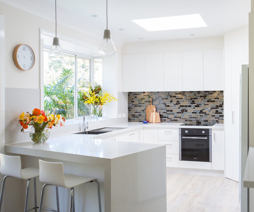 Photo of a mid-sized contemporary l-shaped eat-in kitchen in Other with flat-panel cabinets, white cabinets, with island, an undermount sink, quartz benchtops, grey splashback, glass tile splashback, stainless steel appliances and medium hardwood floors.