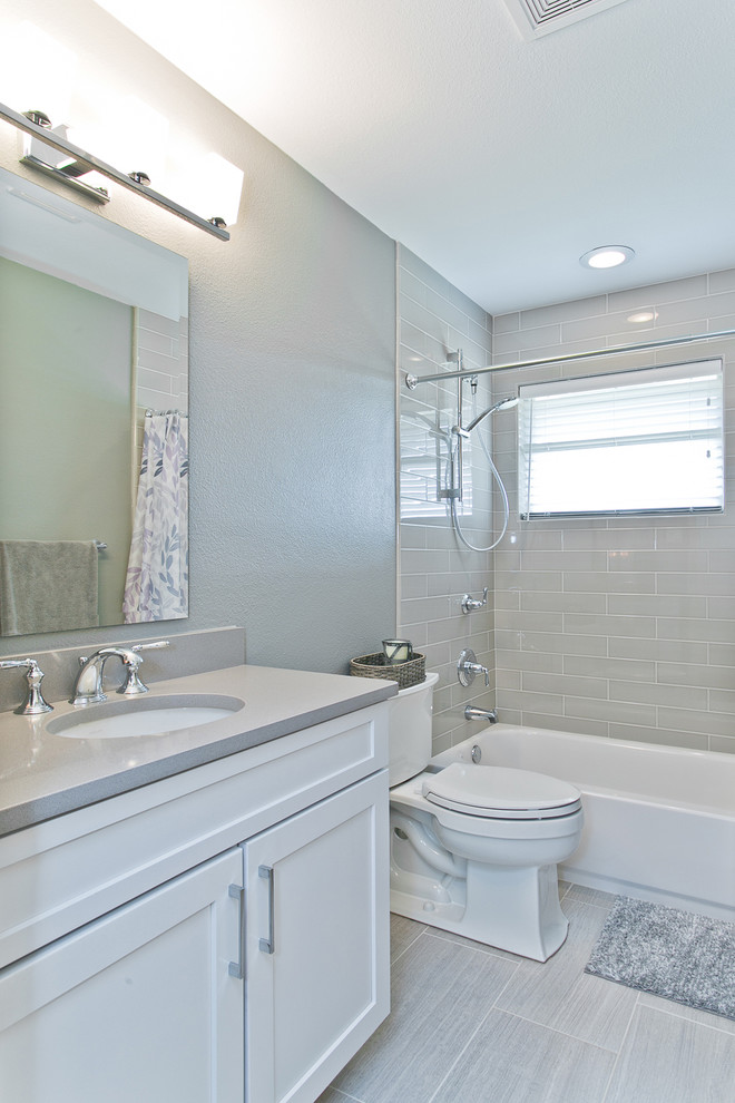 Photo of a mid-sized transitional 3/4 bathroom in Dallas with an undermount sink, raised-panel cabinets, white cabinets, solid surface benchtops, an alcove tub, a two-piece toilet, gray tile, subway tile, grey walls, porcelain floors and a shower/bathtub combo.