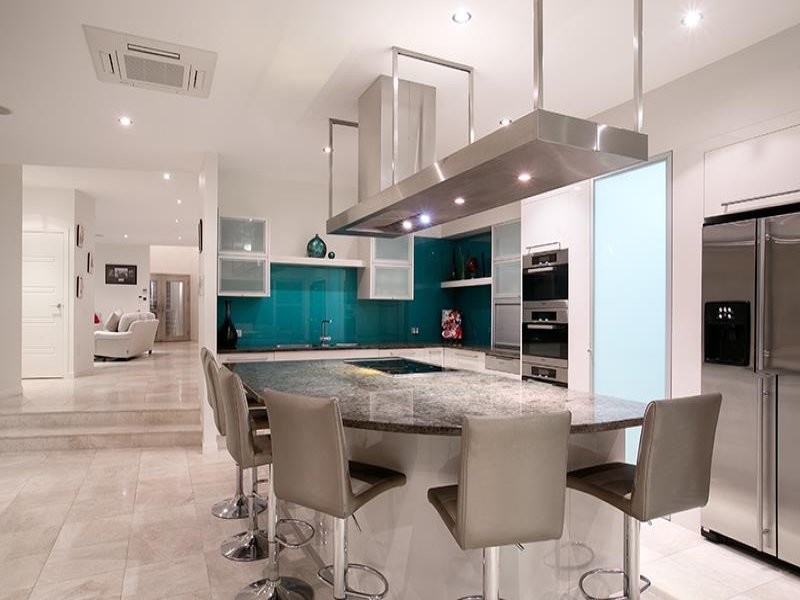 Photo of a large modern l-shaped kitchen in Brisbane with a double-bowl sink, flat-panel cabinets, white cabinets, granite benchtops, blue splashback, glass sheet splashback, stainless steel appliances, travertine floors, with island and multi-coloured floor.