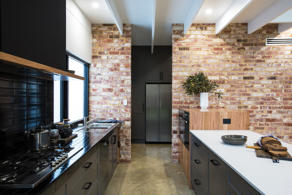 Photo of an expansive industrial galley kitchen pantry in Other with a double-bowl sink, shaker cabinets, grey cabinets, solid surface benchtops, black splashback, subway tile splashback, stainless steel appliances, concrete floors, with island, grey floor and white benchtop.