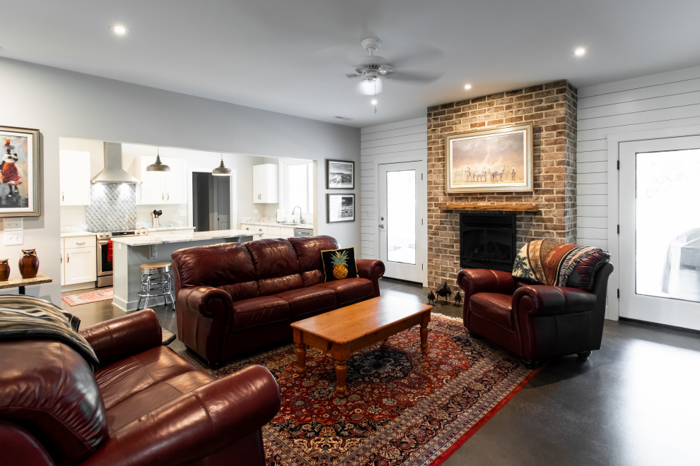 Inspiration for a transitional open concept living room in Charleston with grey walls, concrete floors, a standard fireplace, a brick fireplace surround, a wall-mounted tv and grey floor.