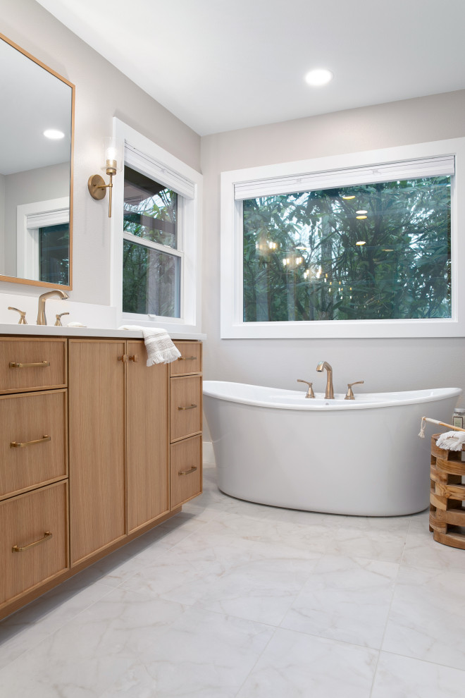 This is an example of an expansive transitional master bathroom in Portland with furniture-like cabinets, light wood cabinets, a freestanding tub, an alcove shower, a one-piece toilet, white tile, porcelain tile, white walls, porcelain floors, an undermount sink, engineered quartz benchtops, white floor, a hinged shower door, white benchtops, an enclosed toilet, a double vanity and a built-in vanity.