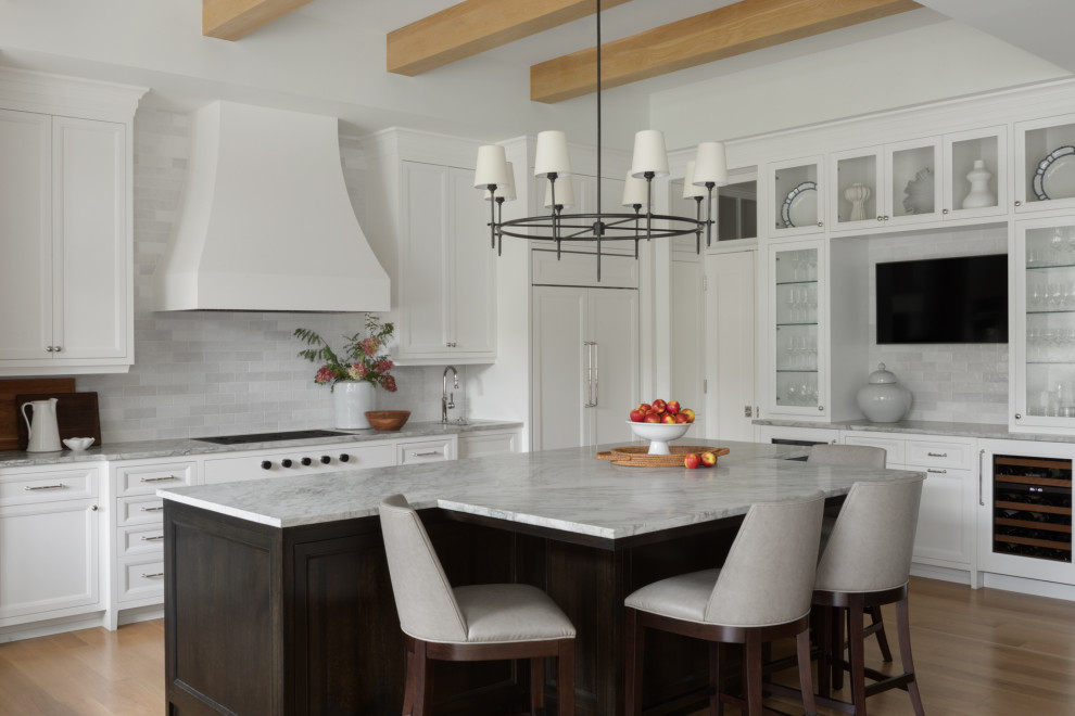 Photo of a rural u-shaped kitchen/diner in Milwaukee with recessed-panel cabinets, white cabinets, quartz worktops, white splashback, stone tiled splashback, integrated appliances, light hardwood flooring, an island, brown floors, grey worktops and exposed beams.