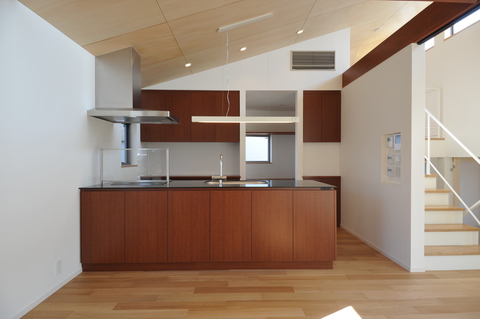 Photo of a small contemporary single-wall open plan kitchen in Tokyo with an undermount sink, flat-panel cabinets, brown cabinets, solid surface benchtops, black appliances, plywood floors, a peninsula, brown floor and black benchtop.