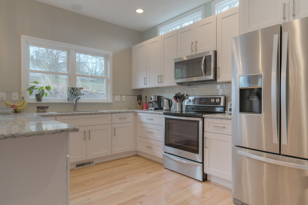 Inspiration for a mid-sized transitional u-shaped light wood floor eat-in kitchen remodel with an undermount sink, shaker cabinets, white cabinets, quartz countertops, beige backsplash, glass tile backsplash, stainless steel appliances and a peninsula