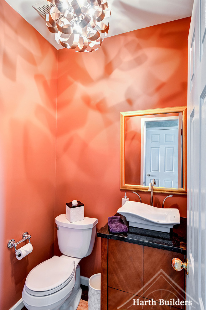 This is an example of a small eclectic powder room in Philadelphia with flat-panel cabinets, medium wood cabinets, a two-piece toilet, orange walls, light hardwood floors, a vessel sink and granite benchtops.