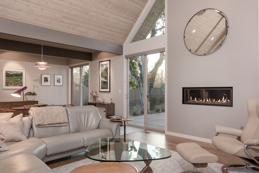 Inspiration for a large midcentury enclosed family room in Portland with white walls, light hardwood floors, a ribbon fireplace, a plaster fireplace surround, a built-in media wall and beige floor.