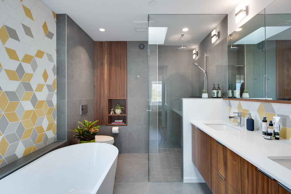 Contemporary bathroom in Vancouver with flat-panel cabinets, medium wood cabinets, a freestanding tub, a curbless shower, gray tile, white tile, yellow tile, mosaic tile, grey walls, an undermount sink, grey floor, a hinged shower door and white benchtops.
