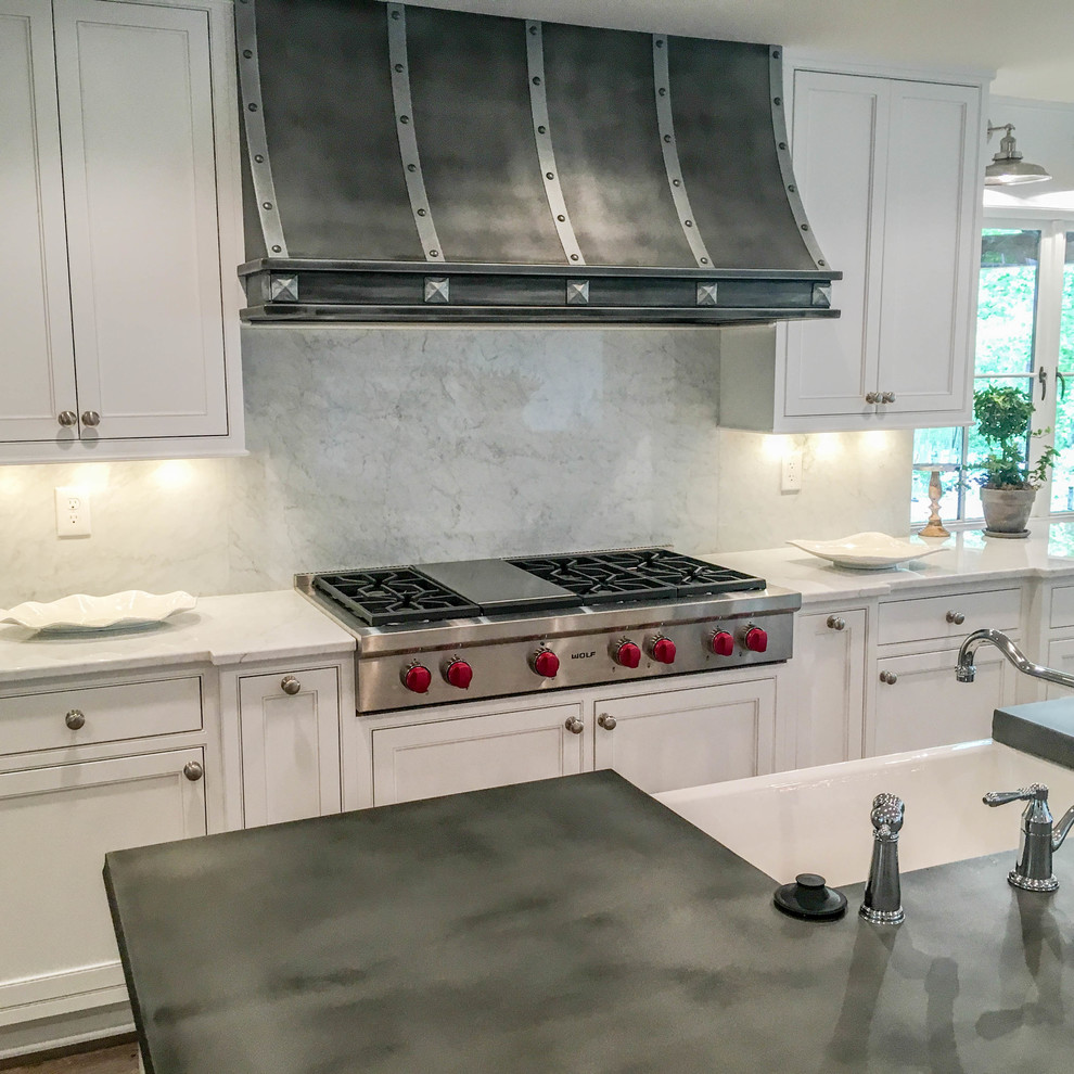 This is an example of an expansive transitional l-shaped kitchen in Other with a farmhouse sink, beaded inset cabinets, white cabinets, zinc benchtops, white splashback, marble splashback, stainless steel appliances, light hardwood floors, multiple islands and brown floor.