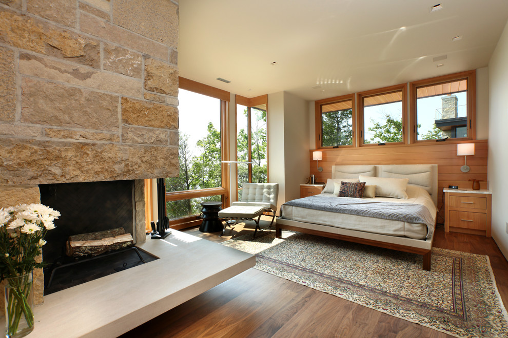 Large contemporary master bedroom in Grand Rapids with white walls, dark hardwood floors, a corner fireplace, a stone fireplace surround and brown floor.