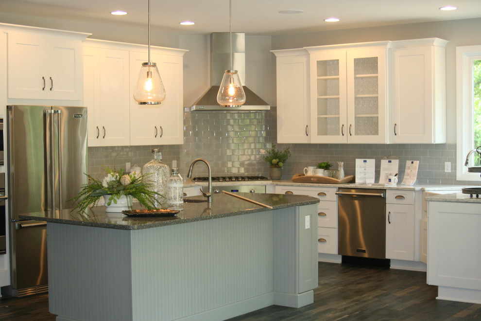 Inspiration for a mid-sized beach style l-shaped eat-in kitchen in Grand Rapids with a drop-in sink, flat-panel cabinets, white cabinets, granite benchtops, grey splashback, subway tile splashback, stainless steel appliances, medium hardwood floors and with island.