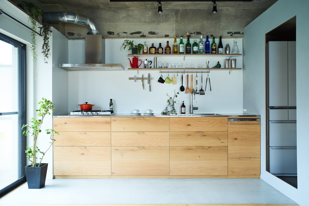 This is an example of an industrial single-wall open plan kitchen in Other with a single-bowl sink, flat-panel cabinets, medium wood cabinets, stainless steel benchtops, white splashback, concrete floors and grey floor.