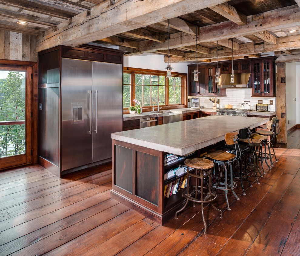 Inspiration for a large country l-shaped kitchen in Detroit with a farmhouse sink, concrete benchtops, white splashback, subway tile splashback, stainless steel appliances, with island, grey benchtop, glass-front cabinets, dark wood cabinets and medium hardwood floors.
