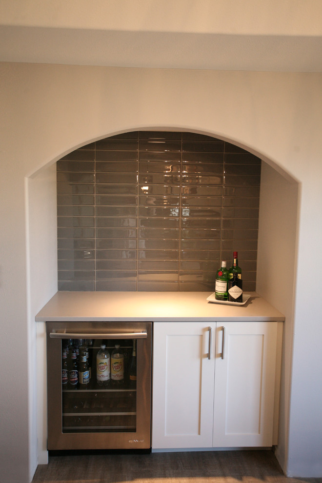 Design ideas for a small transitional single-wall wet bar in Other with no sink, shaker cabinets, white cabinets, solid surface benchtops, grey splashback, glass tile splashback and medium hardwood floors.