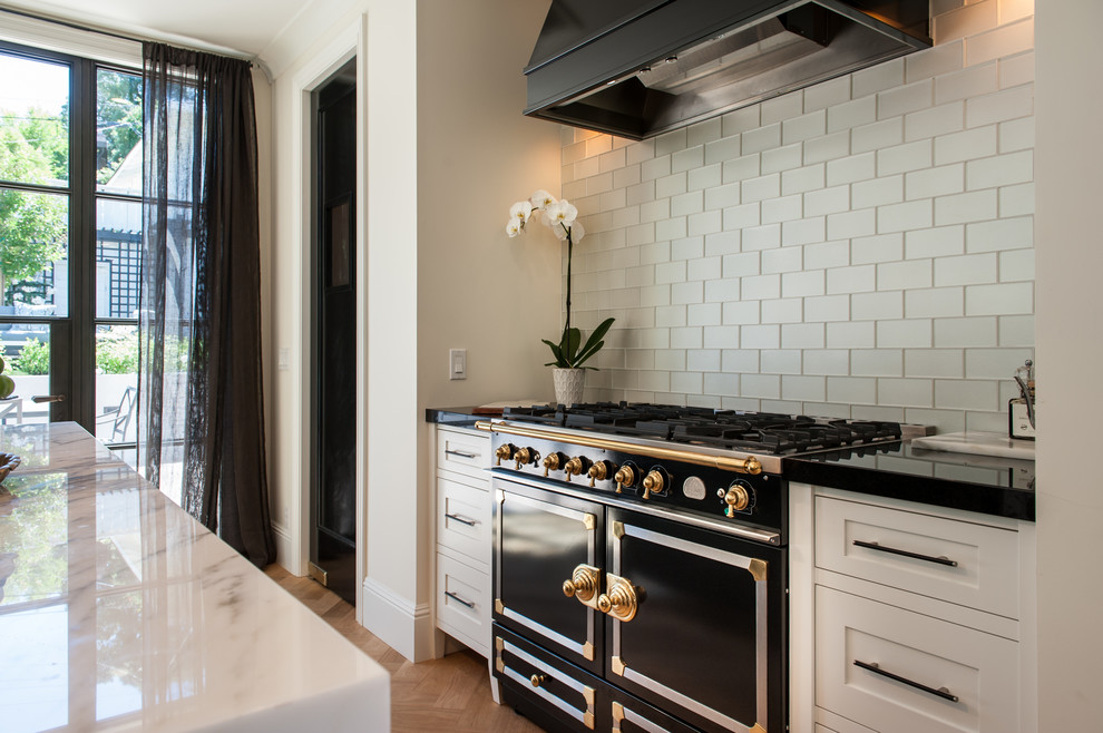Inspiration for a mid-sized traditional galley open plan kitchen in San Francisco with an undermount sink, shaker cabinets, white cabinets, onyx benchtops, beige splashback, subway tile splashback, white appliances, medium hardwood floors and with island.