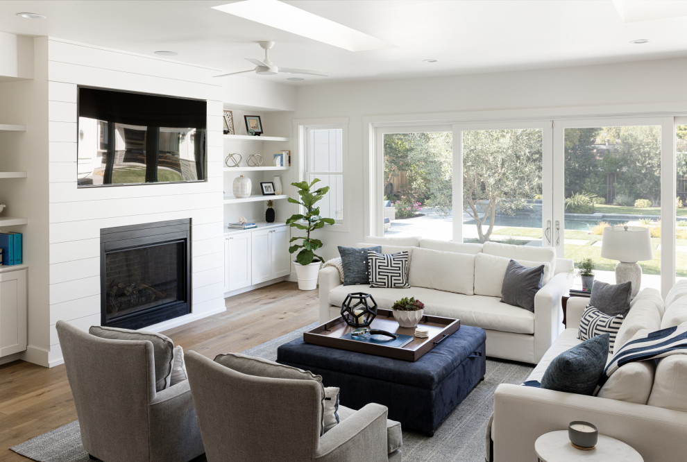 This is an example of a large transitional open concept living room in San Francisco with white walls, medium hardwood floors, a standard fireplace, a metal fireplace surround, a wall-mounted tv and beige floor.