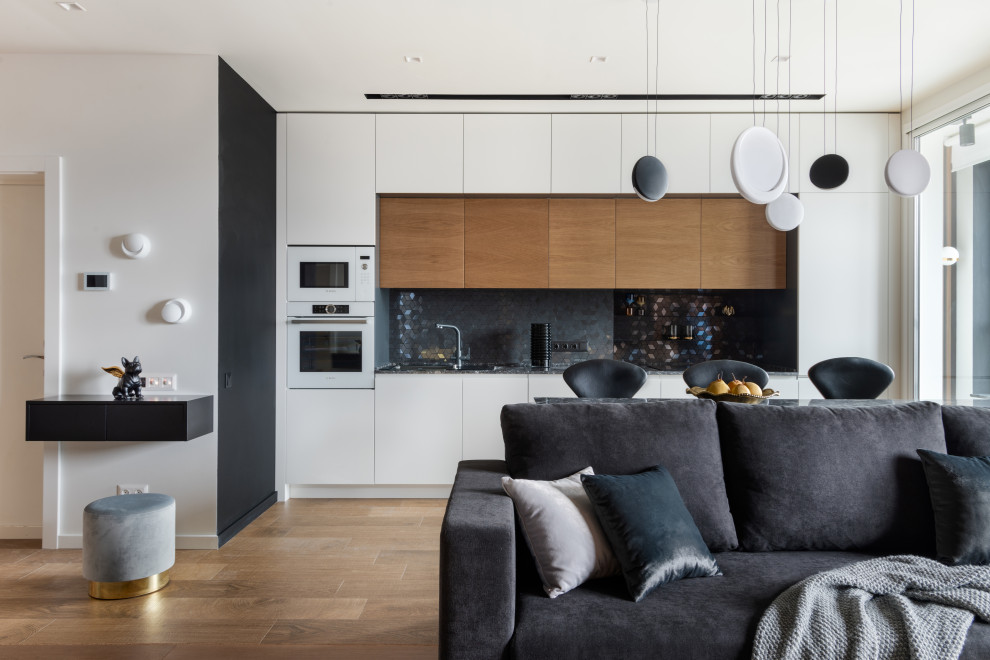 Contemporary single-wall open plan kitchen in Moscow with flat-panel cabinets, white cabinets, black splashback, white appliances, brown floor and black benchtop.