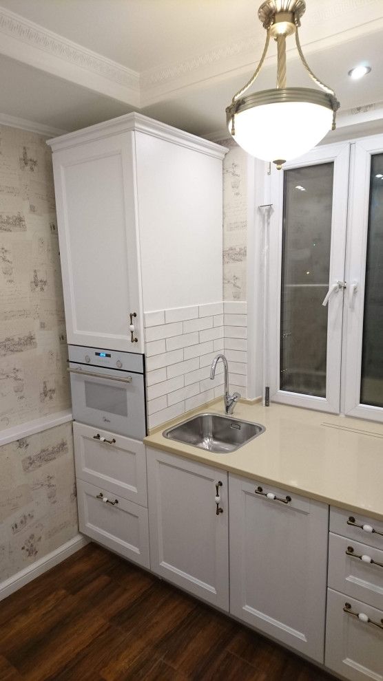 Photo of a small contemporary l-shaped eat-in kitchen in Moscow with a drop-in sink, recessed-panel cabinets, white cabinets, solid surface benchtops, white splashback, subway tile splashback, white appliances, terra-cotta floors, brown floor, beige benchtop and recessed.