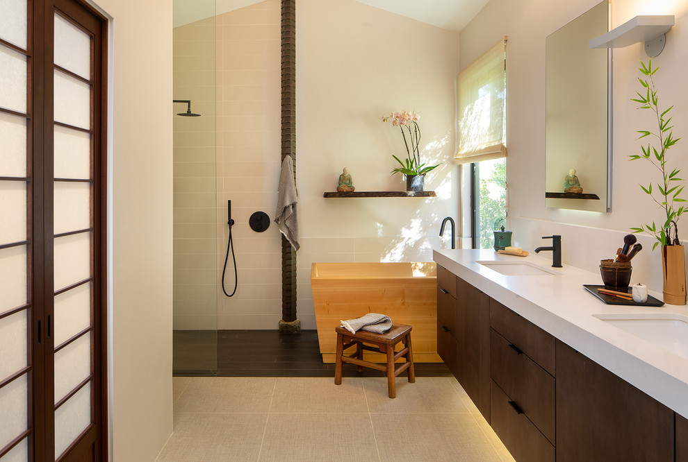 Photo of a large asian master bathroom in San Diego with flat-panel cabinets, medium wood cabinets, a japanese tub, a curbless shower, a two-piece toilet, white tile, porcelain floors, an undermount sink, solid surface benchtops, beige floor, white benchtops, white walls, a double vanity, a built-in vanity, vaulted and an open shower.
