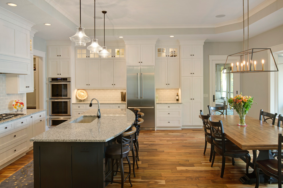 Photo of a large transitional kitchen in Minneapolis with an undermount sink, recessed-panel cabinets, white cabinets, white splashback, subway tile splashback, stainless steel appliances, medium hardwood floors and with island.