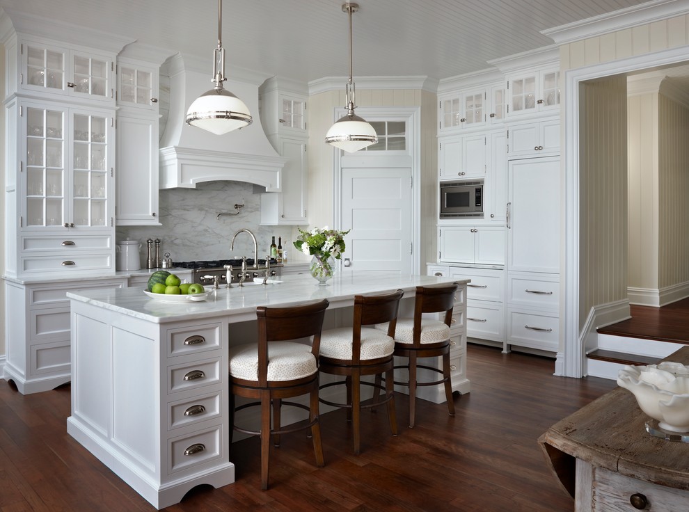 Design ideas for a mid-sized beach style u-shaped kitchen pantry in Other with a farmhouse sink, white cabinets, marble benchtops, white splashback, stone slab splashback, panelled appliances, dark hardwood floors, with island and recessed-panel cabinets.