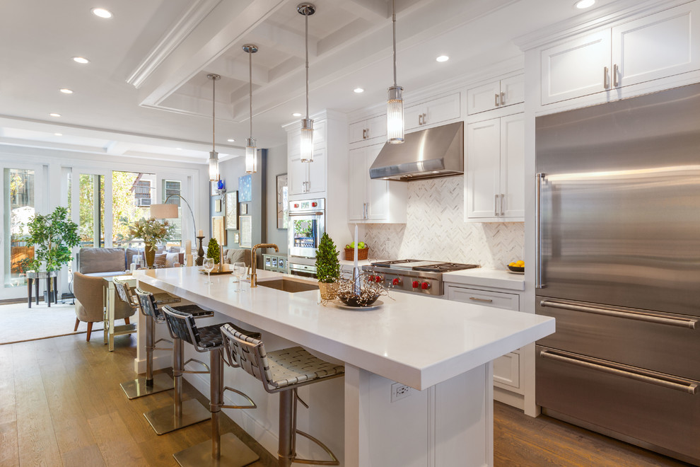 This is an example of a transitional galley open plan kitchen in New York with an undermount sink, recessed-panel cabinets, white cabinets, white splashback, stainless steel appliances, medium hardwood floors and with island.