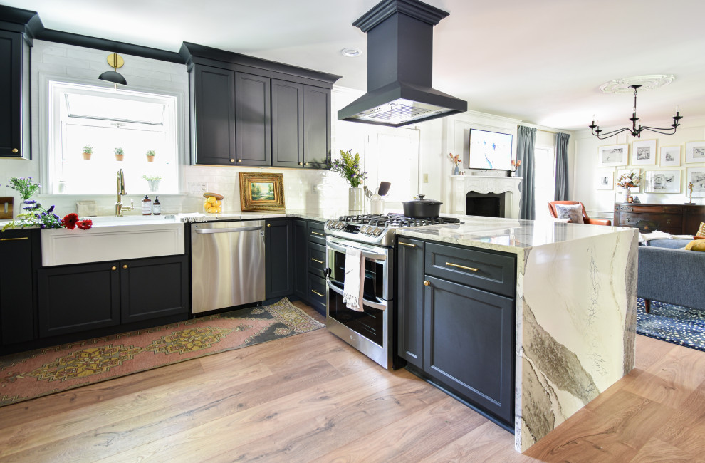 Example of a mid-sized transitional u-shaped laminate floor open concept kitchen design with a farmhouse sink, black cabinets, quartzite countertops, white backsplash and a peninsula