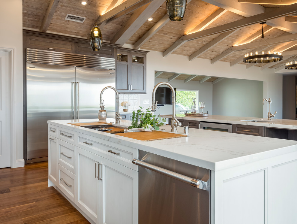 Photo of a large country galley open plan kitchen in Los Angeles with quartz benchtops, multi-coloured splashback, stainless steel appliances, medium hardwood floors, multiple islands, an undermount sink, raised-panel cabinets, dark wood cabinets, cement tile splashback, brown floor and white benchtop.
