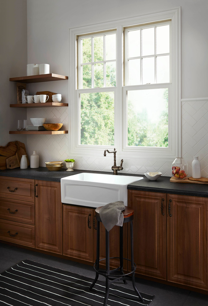 Design ideas for a mid-sized country single-wall open plan kitchen in Orange County with a farmhouse sink, raised-panel cabinets, dark wood cabinets, soapstone benchtops, white splashback, subway tile splashback, stainless steel appliances, slate floors, no island and grey floor.