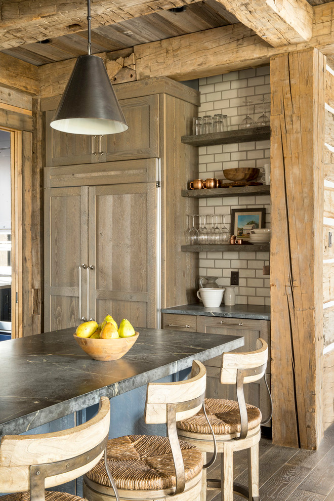 Inspiration for a large rustic u-shaped dark wood floor and brown floor eat-in kitchen remodel in Minneapolis with an undermount sink, shaker cabinets, medium tone wood cabinets, soapstone countertops, white backsplash, ceramic backsplash, paneled appliances and an island